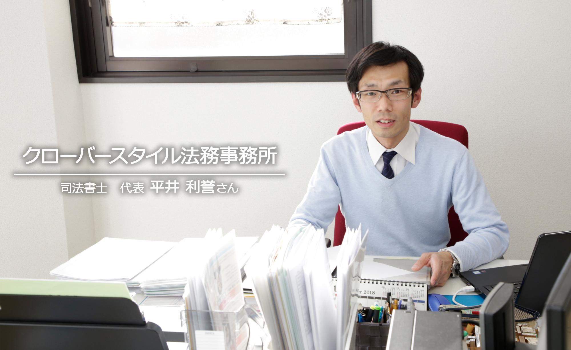 事務所のデスク前に座って仕事をしている、クローバースタイルの代表、司法書士の平井誉士さんを写した写真。