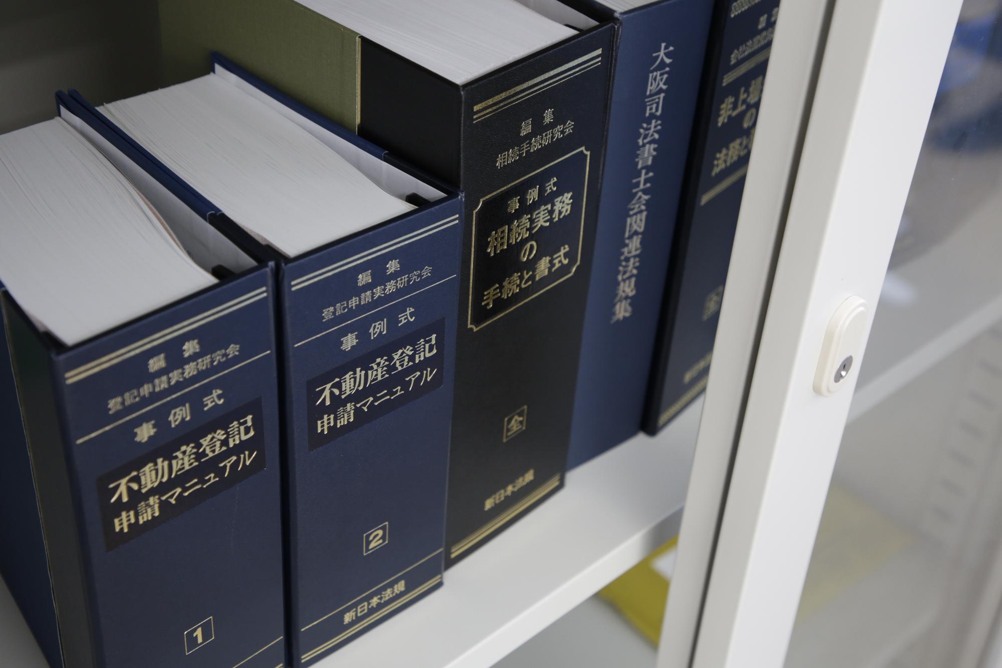 不動産登記申請マニュアルなど、司法書士の仕事に必要な本が棚に並んでいる様子を写した写真。